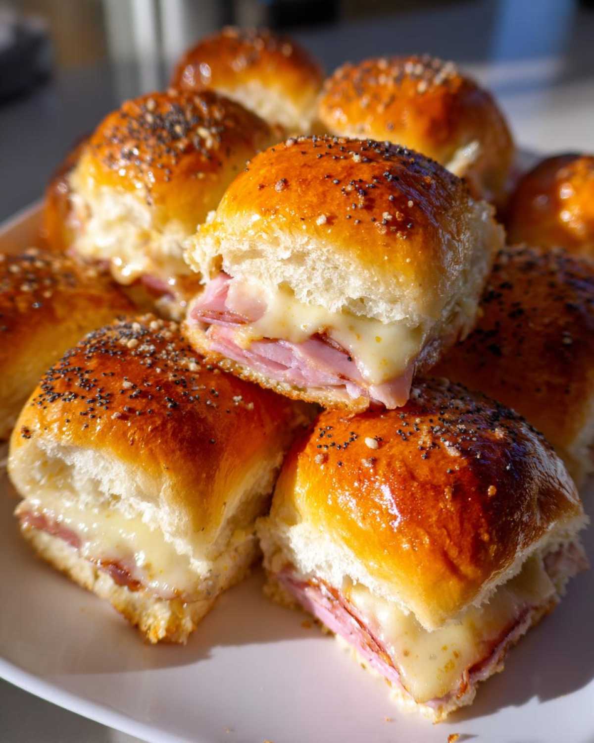 Close-up of several baked Ham and Cheese Sliders with melted cheese oozing out, topped with poppy seeds.