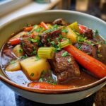 Close-up of a hearty bowl of vegetable beef soup featuring tender beef chunks, large carrots, potatoes, and celery, garnished with parsley.