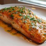 A close-up of a perfectly cooked salmon fillet glazed with honey garlic butter and topped with fresh parsley.