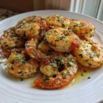 Close-up of juicy, butter-garlic seasoned air fryer shrimp piled on a white plate, ready to eat.