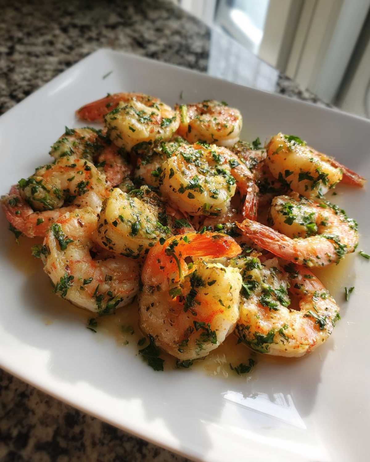 A plate of juicy, cooked air fryer shrimp seasoned generously with chopped parsley and garlic butter.