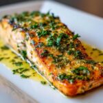 Close-up of a perfectly cooked baked salmon recipe fillet topped with bright green herbs and butter sauce.