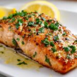 Close-up of a perfectly cooked baked salmon recipe fillet topped with herbs and lemon butter sauce.