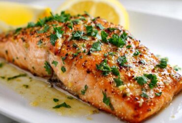 Close-up of a perfectly cooked baked salmon recipe fillet topped with herbs and lemon butter sauce.