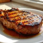 A thick, grilled pork chop glistening with a rich marinade for pork chops glaze, resting on a white plate.