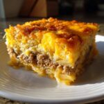 A thick, golden slice of make-ahead egg bake featuring layers of hash browns, ground meat, and melted cheese.