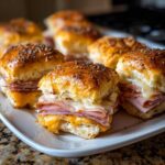 Close-up of freshly baked Ham and Cheese Sliders with melted cheese and poppy seed topping on a white platter.