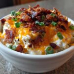 A close-up of rich Million Dollar Dip topped with shredded cheddar cheese, bacon bits, and green onions.