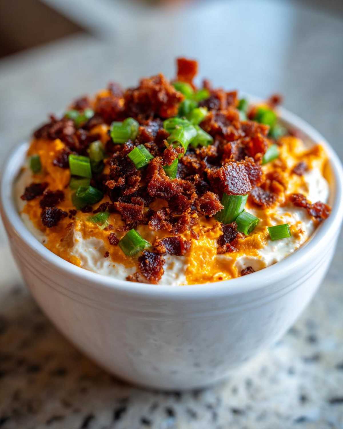 A close-up of rich, creamy million dollar dip topped generously with crispy bacon bits and fresh green onions.