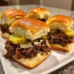 Close-up of four delicious Mississippi pot roast sliders topped with melted cheese and dill pickle slices on soft rolls.