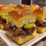 Close-up of several Mississippi pot roast sliders filled with shredded beef, pickles, and onions on sweet rolls.