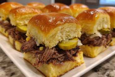 Close-up of several Mississippi pot roast sliders filled with shredded beef, pickles, and onions on sweet rolls.