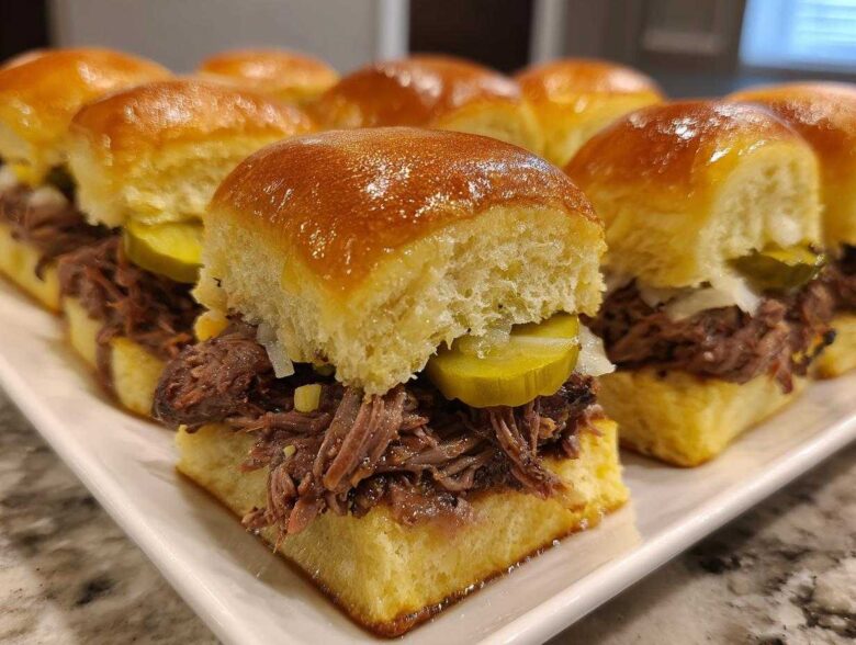 Close-up of several Mississippi pot roast sliders filled with shredded beef, pickles, and onions on sweet rolls.