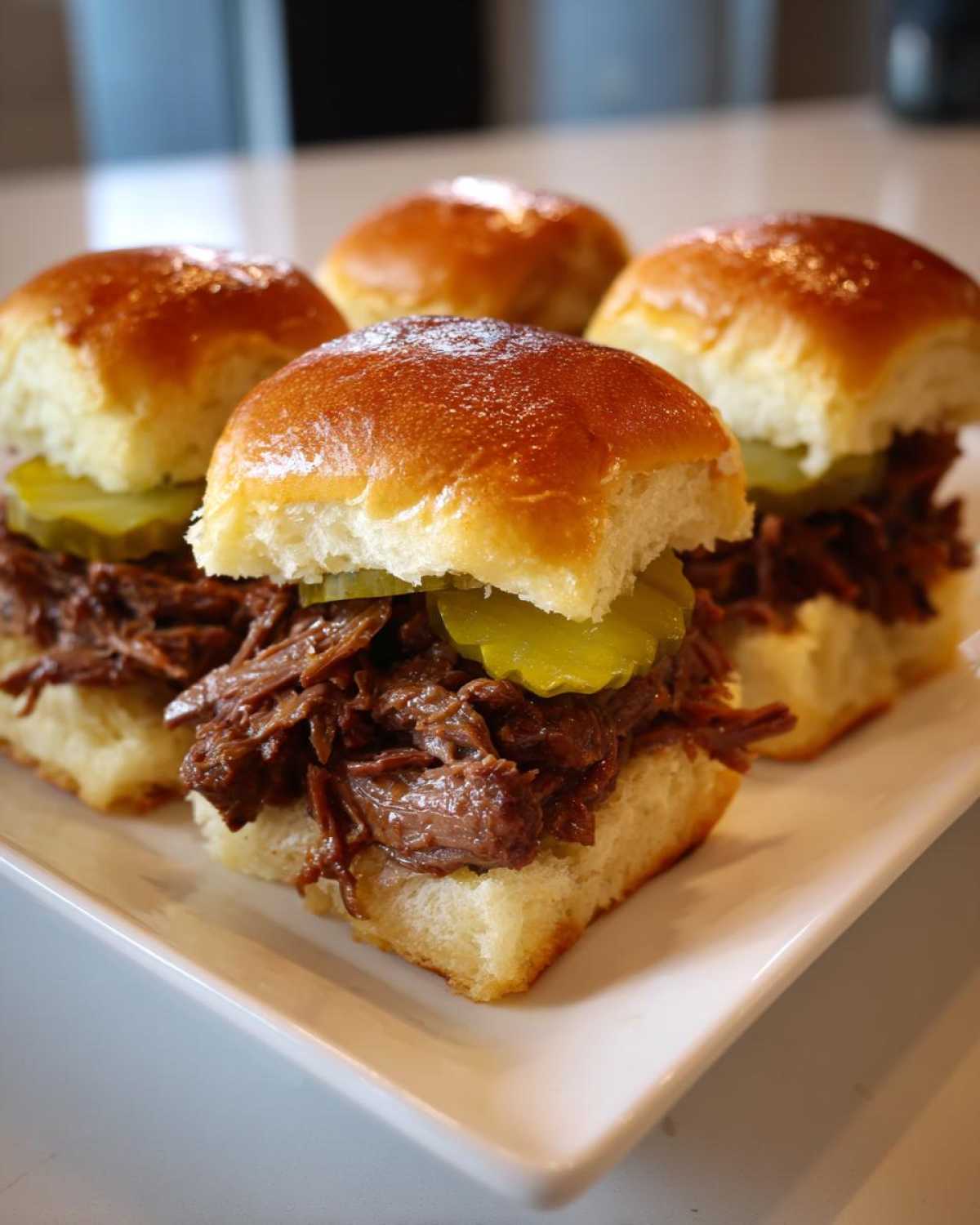 Four delicious Mississippi pot roast sliders piled high with shredded beef and pickle slices on soft buns.