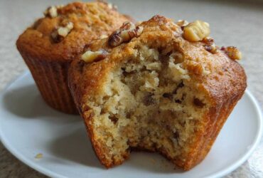 Close-up of moist banana nut muffins, one bitten open to show the texture, topped with walnuts.