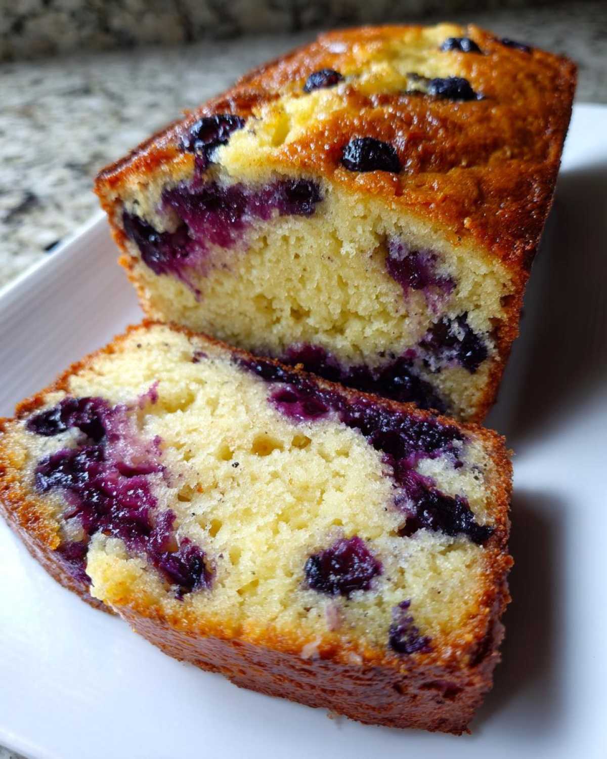Close-up of a thick slice of moist blueberry banana bread showing yellow crumb and purple blueberries.