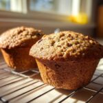 Two freshly baked, moist bran muffins cooling on a wire rack in bright sunlight.