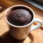 Close-up of a rich, dark chocolate mug cake risen perfectly inside a white ceramic mug.