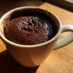 Close-up of a moist chocolate mug cake baked directly in a white ceramic mug, sitting on a wooden surface.