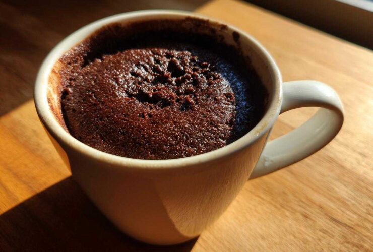 Close-up of a moist chocolate mug cake baked directly in a white ceramic mug, sitting on a wooden surface.