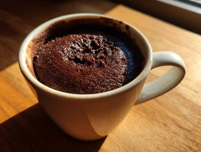 Close-up of a moist chocolate mug cake baked directly in a white ceramic mug, sitting on a wooden surface.