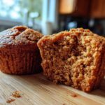 Two rich brown honey bran muffins on a wooden board, one cut in half showing the moist, crumbly texture inside.