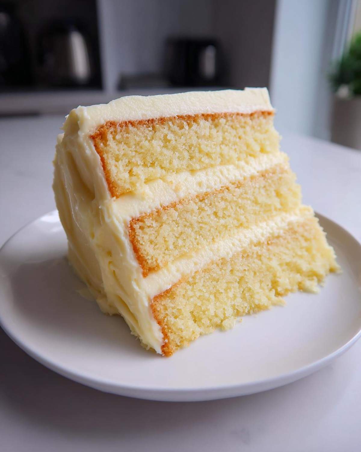 A generous slice of moist vanilla cake recipe showing three layers of yellow cake and creamy white frosting.