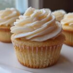 Close-up of a perfectly baked vanilla cupcake topped with swirled white vanilla frosting.