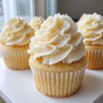 Close-up of a perfectly baked vanilla cupcake topped with high swirls of creamy white vanilla frosting.