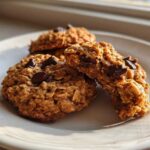 Three delicious oatmeal chocolate chip breakfast cookie treats stacked on a white plate, catching warm sunlight.