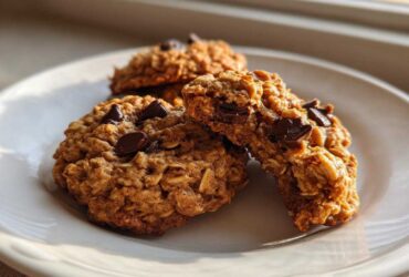 Three delicious oatmeal chocolate chip breakfast cookie treats stacked on a white plate, catching warm sunlight.