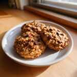 Three freshly baked, textured oatmeal cookie studded with chocolate chips resting on a light gray plate.