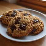 Four freshly baked chocolate chip oatmeal cookie stacked slightly on a white plate, showcasing chewy texture.