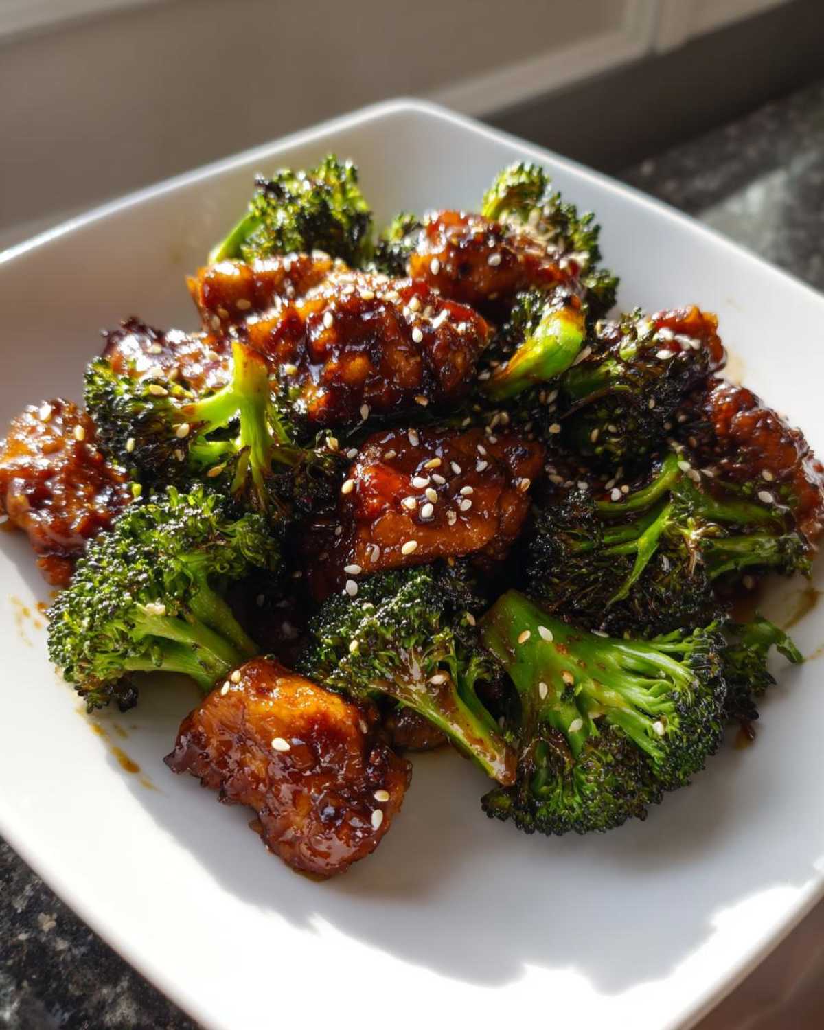 Close-up of glazed chicken and broccoli tossed in sauce and sprinkled with sesame seeds.