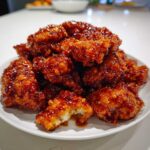 A pile of crispy, glazed pieces of orange chicken recipe coated in a thick, shiny, dark orange sauce.