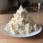 A large mound of perfectly piped, creamy vanilla buttercream frosting on a white plate.