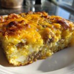 A close-up, sunlit slice of sausage and cheese egg bake showing golden-brown topping and fluffy interior.