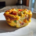 A close-up, cross-section view of a savory Egg Muffin Cup filled with ham and colorful bell peppers.