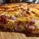 A close-up, cross-section view of cheesy scalloped potatoes and ham baked into a golden-brown casserole.
