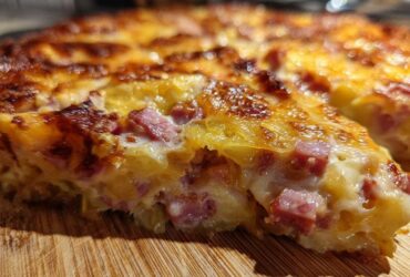 A close-up, cross-section view of cheesy scalloped potatoes and ham baked into a golden-brown casserole.