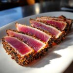 Five slices of perfectly Seared Ahi Tuna, crusted with black and white sesame seeds, showing a rare, deep red center.