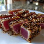 Close-up of perfectly seared ahi tuna slices, crusted with sesame seeds, showing a bright pink center.
