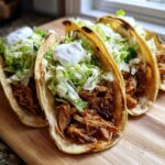 Close-up of three soft shell chicken tacos filled with shredded chicken, lettuce, and sour cream.