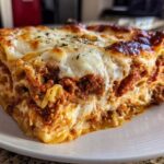 A thick, hearty slice of 9-layer lasagna featuring rich meat sauce and melted, browned cheese topping.
