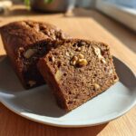 Close-up of a slice of moist date nut bread showing walnuts and dates embedded in the dark brown loaf.