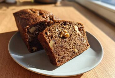 Close-up of a slice of moist date nut bread showing walnuts and dates embedded in the dark brown loaf.