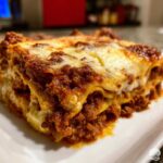 Close-up of a thick slice of rich, layered lasagna featuring meat sauce and melted cheese topping.
