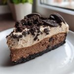 A decadent slice of layered Oreo pie showing a dark crust, chocolate mousse, light mousse, and crushed Oreo topping.