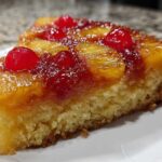 Close-up of a moist slice of pineapple upside down cake topped with caramelized pineapple and maraschino cherries.