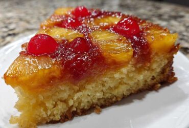 Close-up of a moist slice of pineapple upside down cake topped with caramelized pineapple and maraschino cherries.